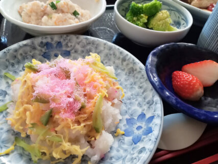 介護施設の食事。桜色の炒飯と副菜、果物が盛られた昼食。